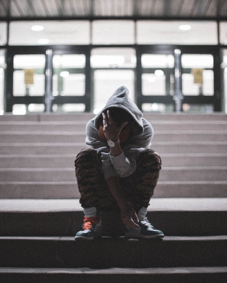 A teenager in a hooded sweatshirt sitting alone on school steps