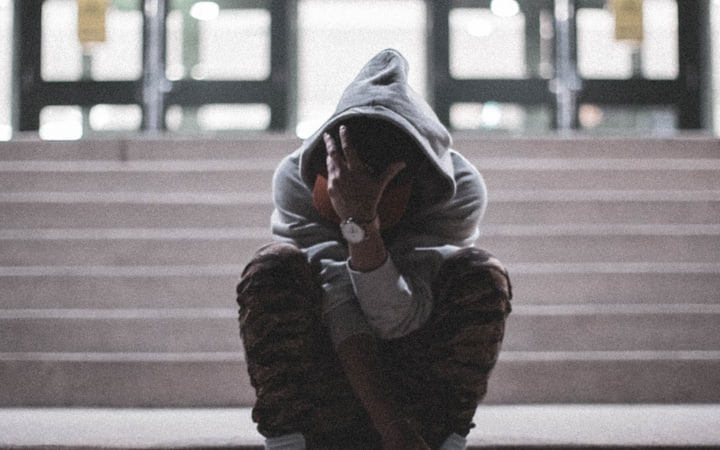 A teenager in a hooded sweatshirt sitting alone on school steps