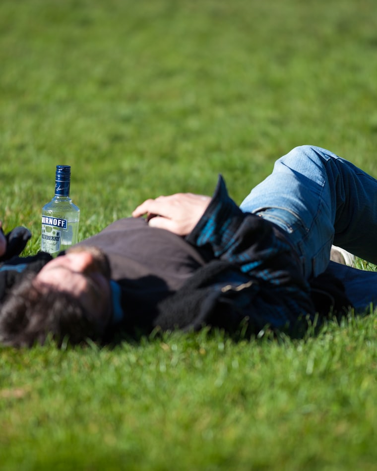 A man lying on the grass beside an empty bottle
