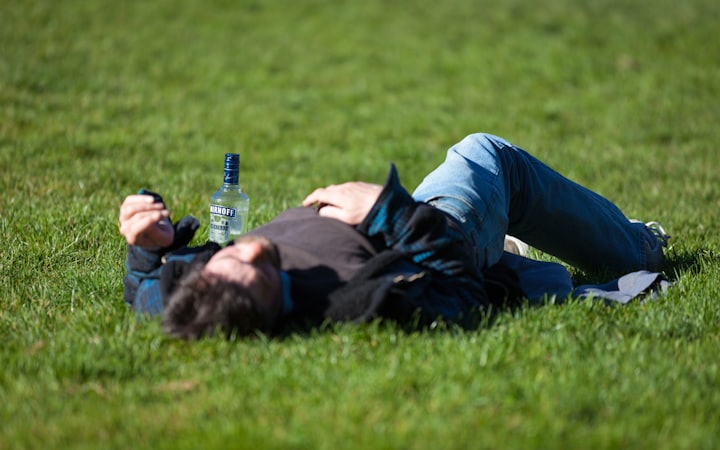 A man lying on the grass beside an empty bottle