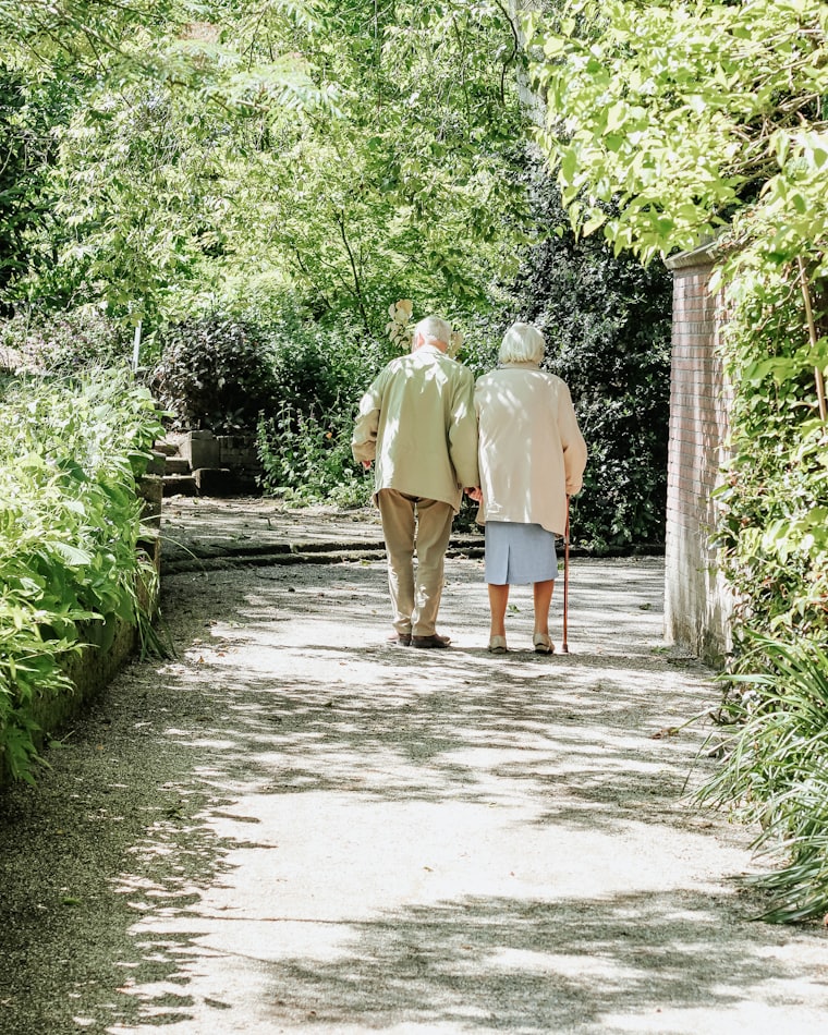 An elderly couple walking arm in arm along a garden path