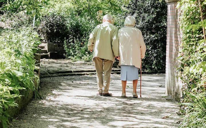 An elderly couple walking arm in arm along a garden path