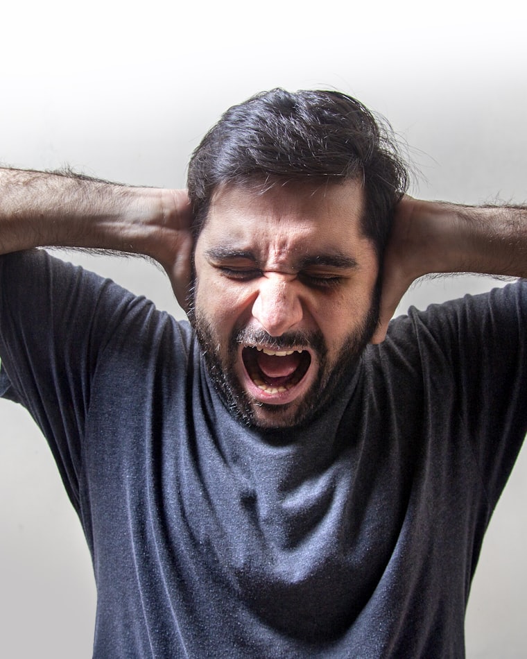 A man in acute distress, hands clamped over his ears