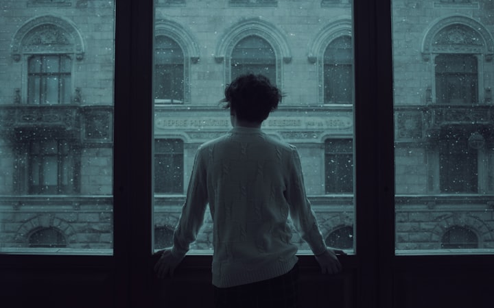 A person standing alone at a dark window, back turned to the room