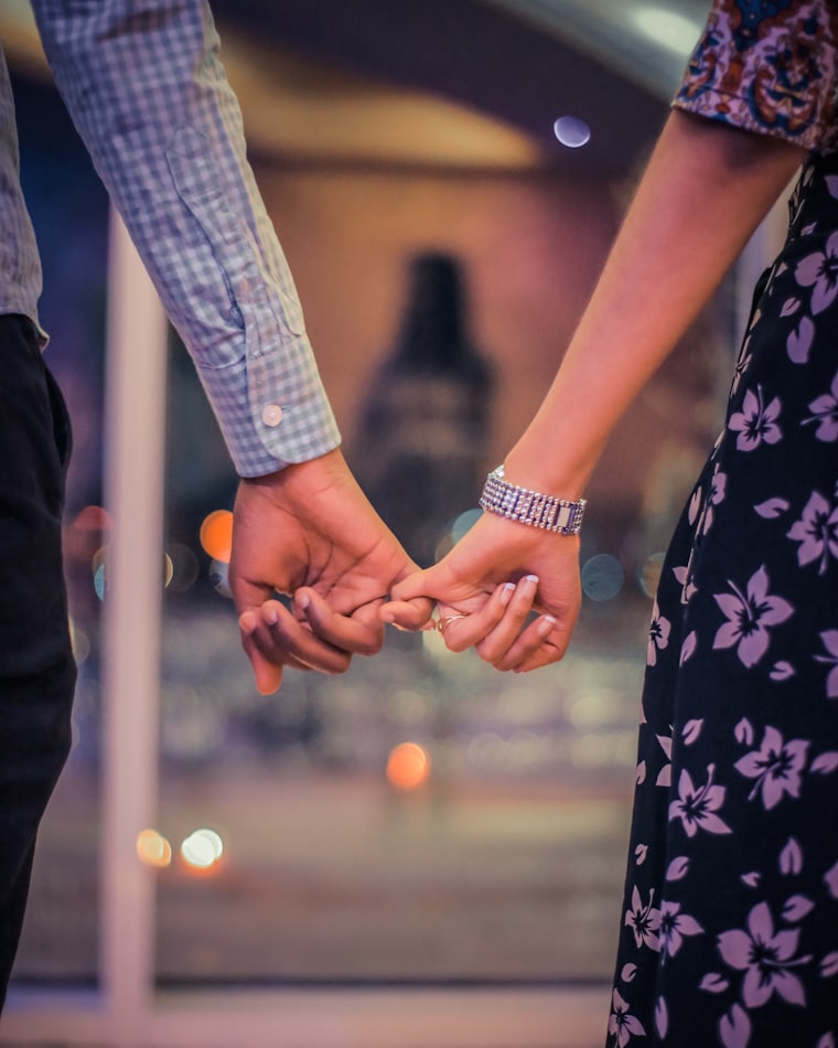 A couple standing together, hands linked by their little fingers