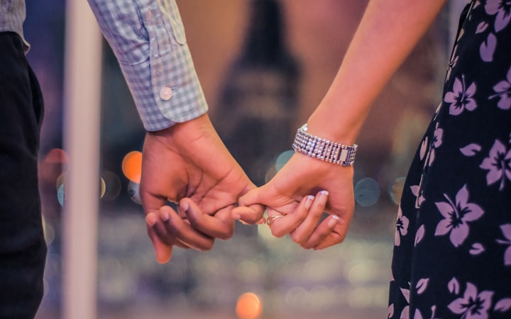 A couple standing together, hands linked by their little fingers